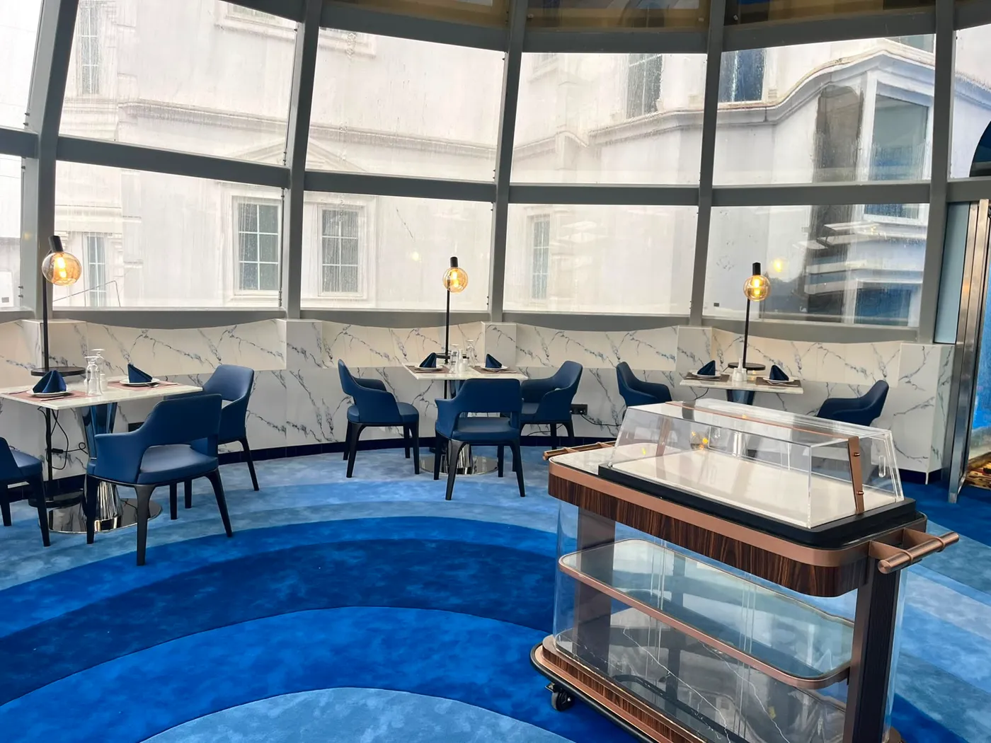 The rosewood-and-glass dessert trolley on the blue carpet of The Eye
